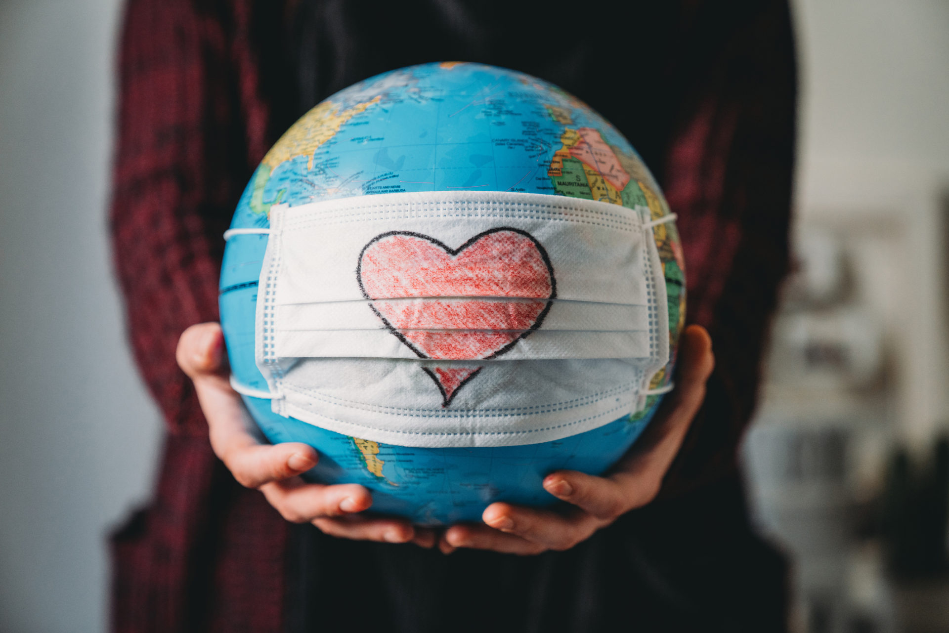 Young woman holding a globe with a face mask on it - Heart shape is drawn on the mask